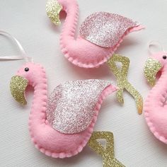 three pink and gold flamingo ornaments on a white table with silver glittered accents