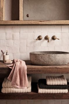 a bathroom sink sitting under a mirror on top of a wooden shelf next to towels