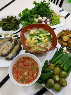 a table topped with plates and bowls filled with different types of food next to veggies