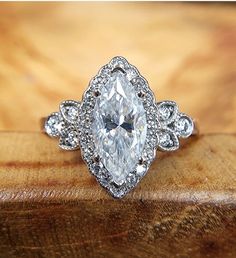 an oval cut diamond surrounded by smaller round diamonds sits on a wooden surface in front of the camera