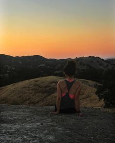 a woman sitting on top of a hill at sunset