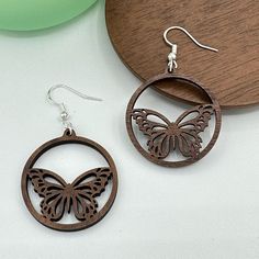 a pair of wooden earrings with a butterfly on the front, and a circular design on the back