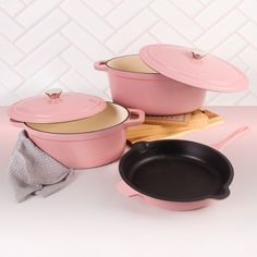 three pink pots and pans sitting on top of a wooden cutting board next to each other