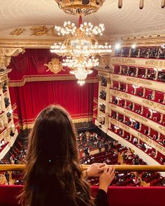 a woman standing in front of an auditorium filled with red velvet seats and chandeliers