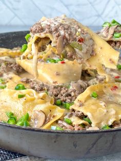 a skillet filled with pasta and meat covered in cheese, green onions and sauce