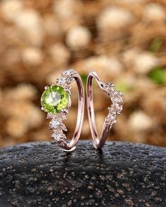 two gold rings with green and white stones on top of a rock in front of some rocks