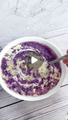 a person holding a spoon in a bowl of purple food on a white wooden table