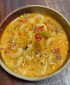 a metal bowl filled with pasta soup on top of a wooden table