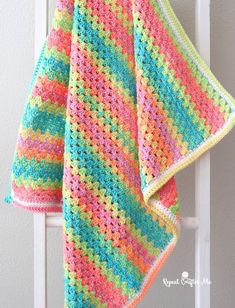 a multicolored crocheted blanket hanging on a white ladder