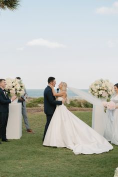 a bride and groom standing in front of their wedding party with the ocean in the background