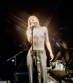 a woman standing on top of a stage next to a drum set and microphone in front of her