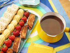 a plate with sandwiches and strawberries next to a cup of coffee on a table