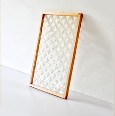 a wooden frame holding a woven piece of cloth on top of a white table next to a wall