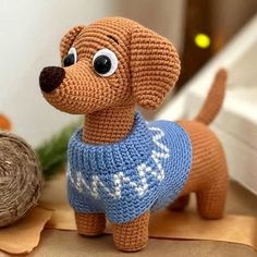 a crocheted toy dog wearing a sweater next to a ball of twine