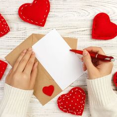 someone is writing on a piece of paper with red hearts around it and two hands holding a pen