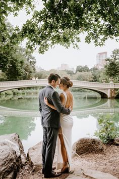 a bride and groom standing next to each other in front of a bridge over water