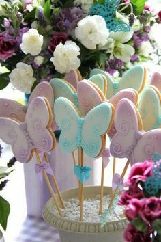 there are many decorated cookies on sticks in the cupcakes holder with purple and white flowers