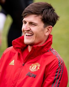 a man in a red jacket smiles at the camera while standing on a soccer field