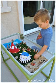 a young boy playing with a toy train set in a play table that is made out of grass