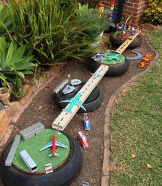 toy airplanes and cars are on display in a garden with fake grass, rocks and flowers