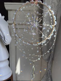 a white horse is standing next to a window with a glass dream catcher hanging from it's side