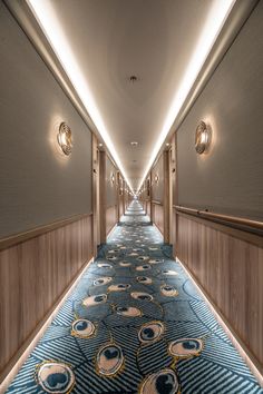 a long hallway with blue carpeting and lights on either side is lit by recessed lighting