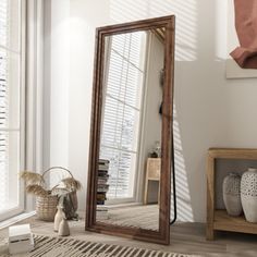 a large mirror sitting on top of a wooden floor next to a vase and potted plant