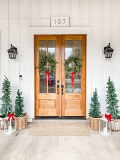 two wooden doors with wreaths and christmas trees in front of them on a porch