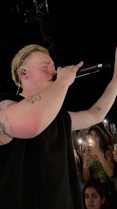 a man with tattoos on his arm holding a microphone in front of a group of people