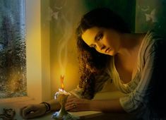 a woman sitting at a table with a candle in her hand and looking out the window