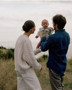 a man holding a baby while standing next to two women and a boy in a field