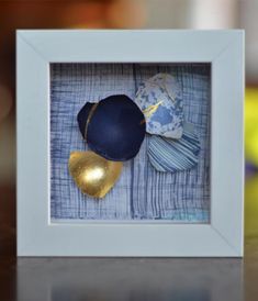 a blue and gold hat is in a white frame on a table with other items