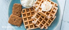 a blue plate topped with waffles and whipped cream next to two small cookies