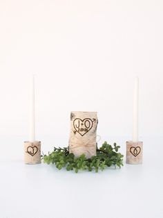 three candles with hearts drawn on them sitting next to some greenery and two white candles