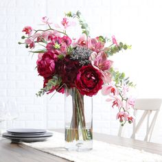 a vase filled with flowers sitting on top of a wooden table next to plates and utensils