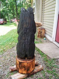 a large wooden bear statue sitting on top of a tree stump in front of a house