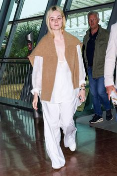 a woman wearing white pants and a brown vest is walking through an airport with another man in the background