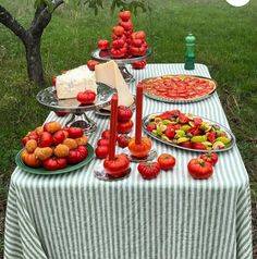 a table topped with lots of food on top of a grass covered field next to trees