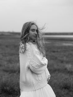 a woman standing in a field with her hair blowing in the wind, black and white photo