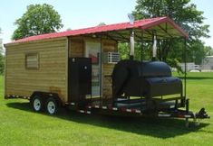 a small house on wheels is parked in the grass with a red roof over it