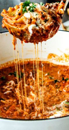 a ladle full of pasta being lifted from a pot with meat and cheese in it