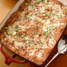 a casserole dish with meat, cheese and green onions in it on a wooden table