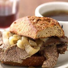 a roast beef sandwich with onions and gravy on a plate next to a cup of coffee