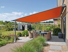 an orange awning over a table and chairs in a courtyard area with plants on the side