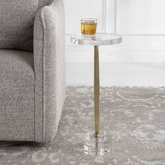 a glass and metal side table with a drink on it in front of a couch