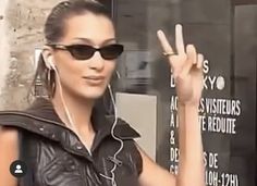 a woman in black leather jacket and sunglasses making the peace sign with her hand while wearing headphones