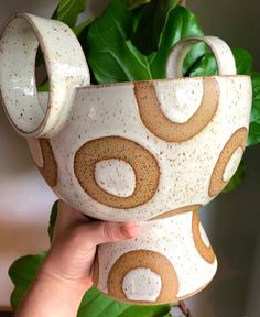 a hand holding a white and brown ceramic vase with circles on it's sides