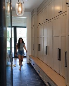 a woman walking through a kitchen with white cabinets and drawers on either side of the counter