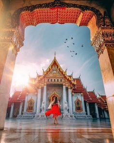 a woman in a red dress is standing under an archway with birds flying around her