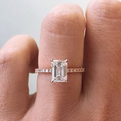 a woman's hand with a diamond ring on top of her finger and an emerald stone in the middle